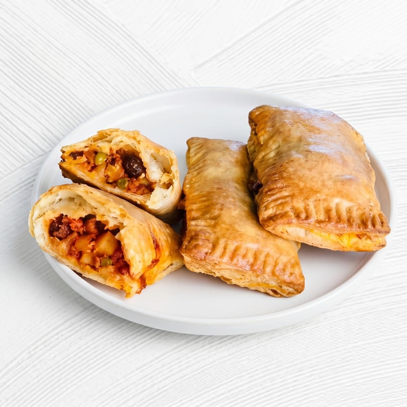 Four golden-brown empanadas on a white plate, two whole and one cut open revealing a savory filling.