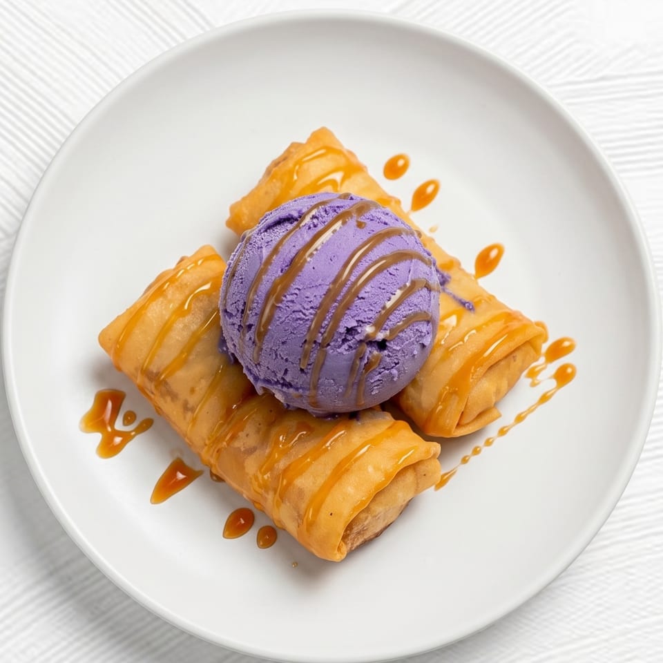 Three golden-fried spring rolls topped with a scoop of purple ice cream and caramel drizzle on a white plate.