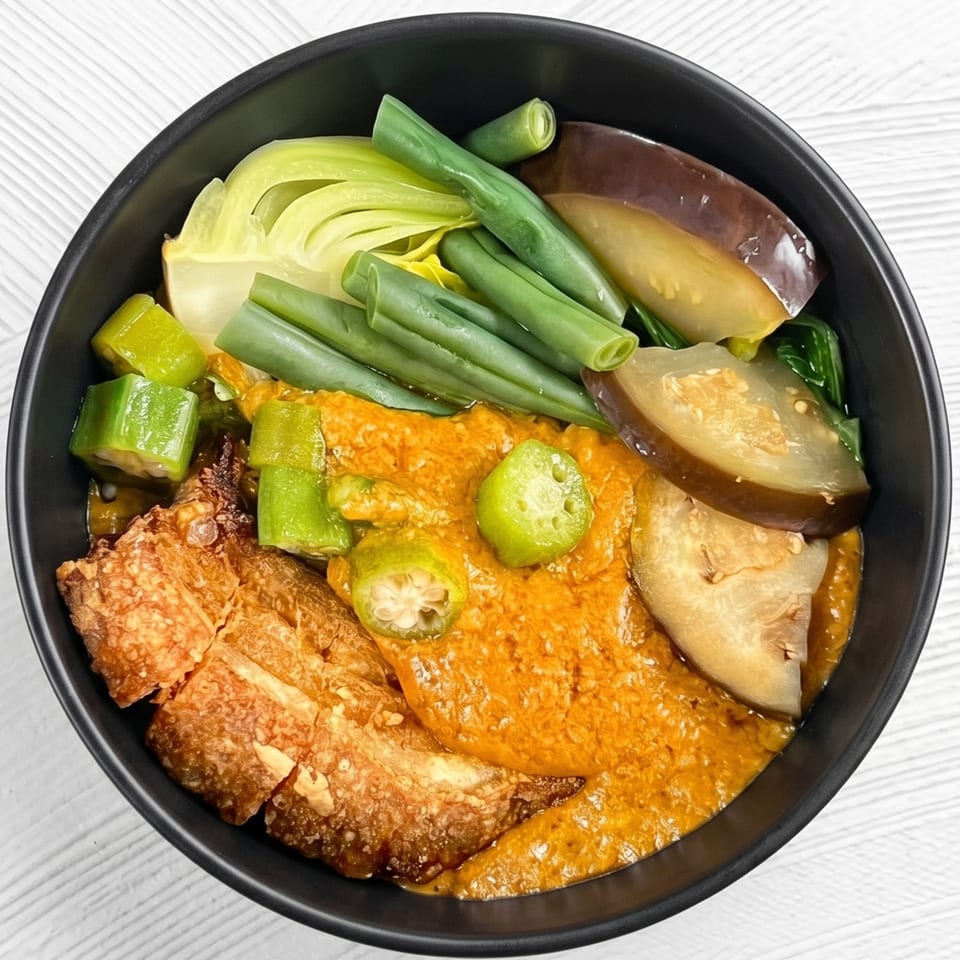 A black bowl filled with kare-kare, featuring crispy pork, green beans, bok choy, eggplant, and okra.